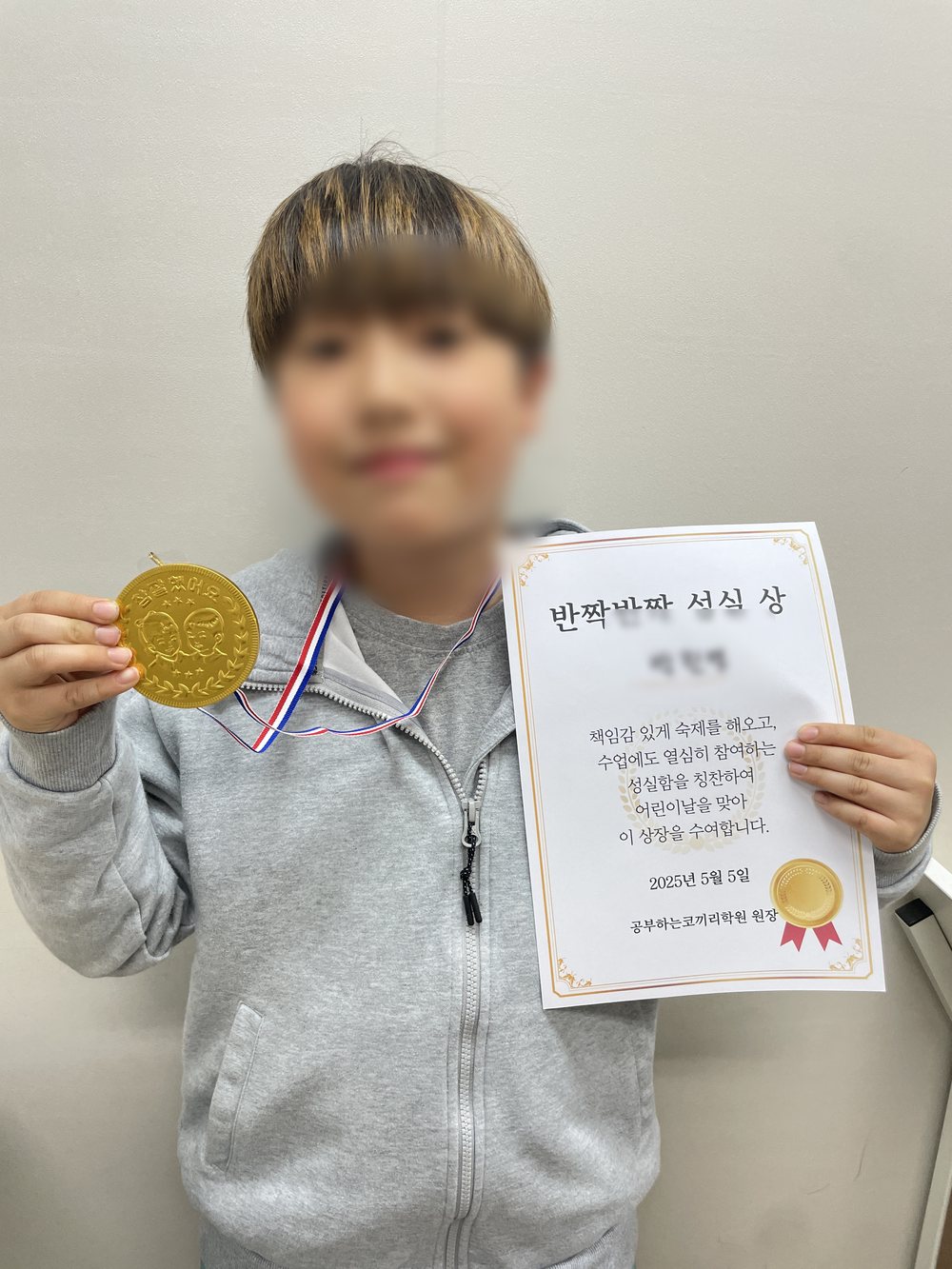 공부하는코끼리수학 학생이 반짝반짝 성실상 상장과 금색 메달을 들고 있다. 상장에는 책임감 있게 숙제를 해오고 수업에도 열심히 참여하는 성실함을 칭찬하여 이 상장을 수여한다고 적혀 있다. 개인정보 보호를 위해 얼굴과 이름은 가렸다.