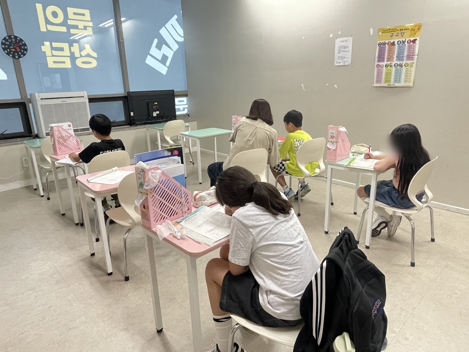 공부하는코끼리수학 초등 3~4학년 교실. 학생들이 한 명씩 떨어져 앉아 각자 다른 교재로 문제를 풀고 있고 벽에 구구단 표가 붙어 있다.