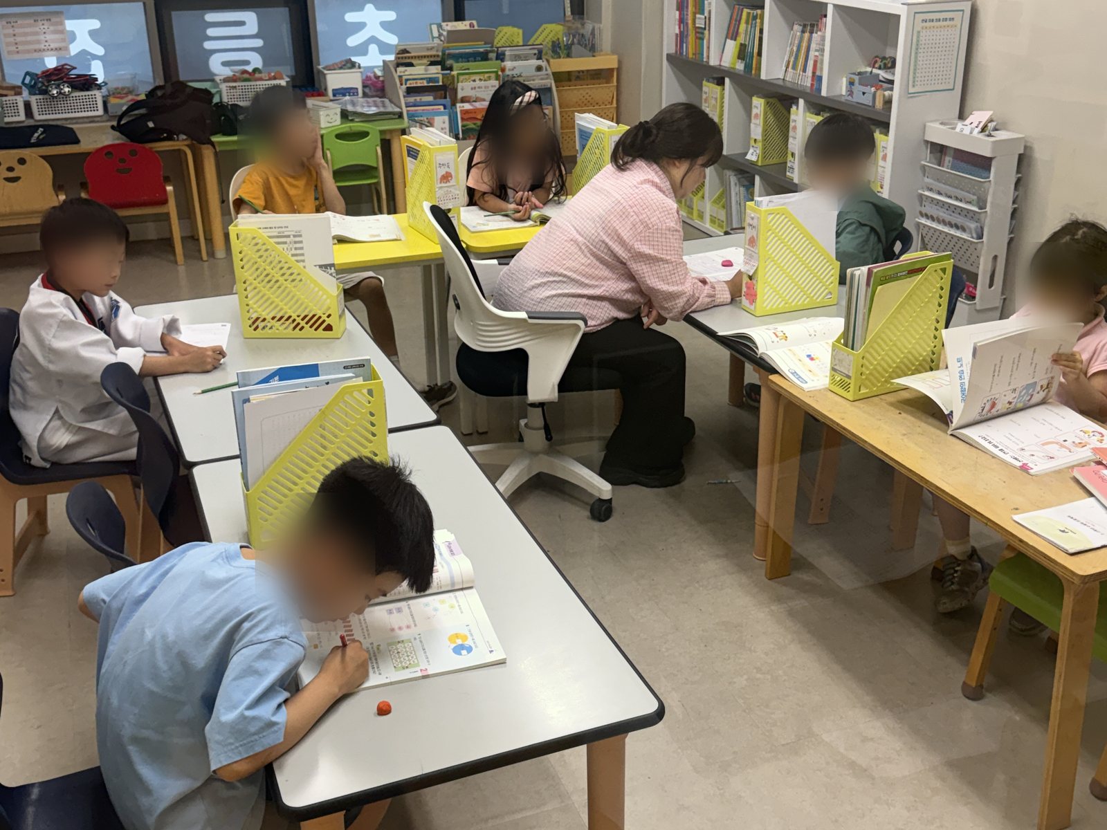 공부하는코끼리수학 저학년 수업 장면. 선생님이 한 아이 옆에 앉아 문제를 함께 보고 있고, 다른 아이들은 각자 다른 교재로 문제를 풀고 있다. 소수정예로 운영한다.